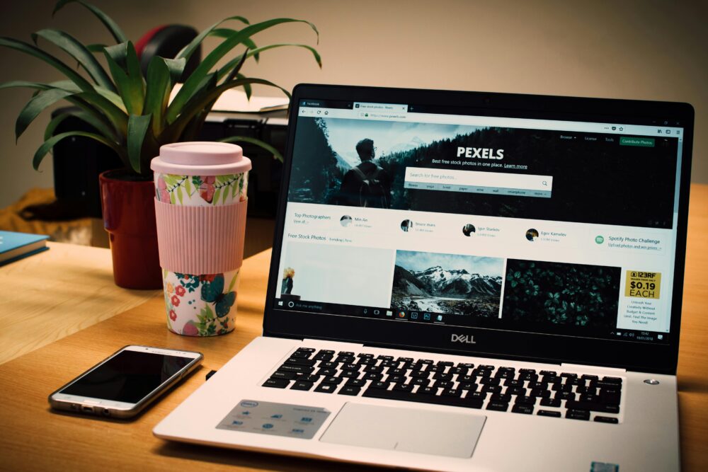 A tidy desk setting with a laptop showing a stock photo website and a smartphone.